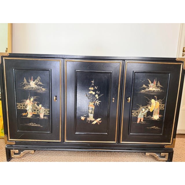 Chinoiserie cabinet with gold leaf and brass hardware details, hand-painted scenes on door panels.