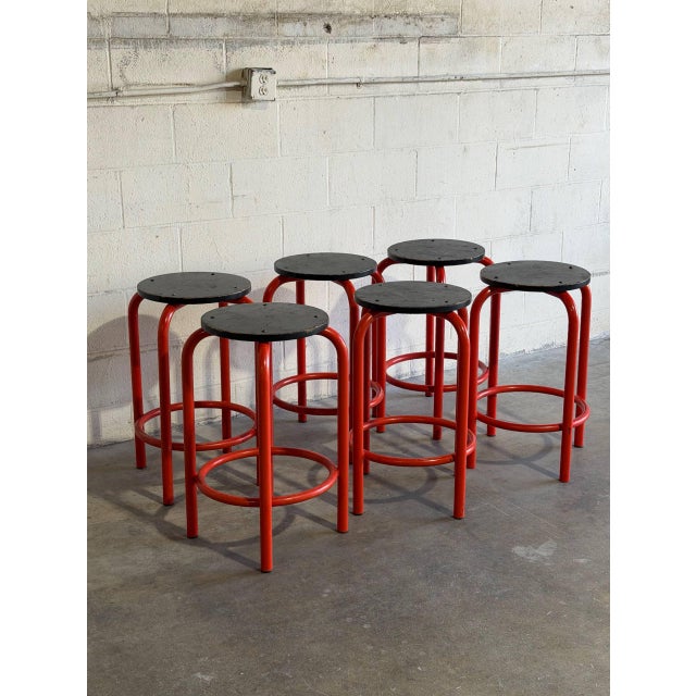 This vibrant set of six bar stools features bold red tubular metal frames paired with dark round seats. The stackable...
