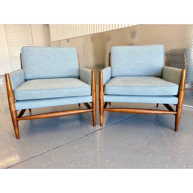 A pair of lounge chairs features a wood frame and light blue upholstery with a distinctive buckle accent straps Both are...