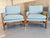 A pair of lounge chairs features a wood frame and light blue upholstery with a distinctive buckle accent straps Both are...
