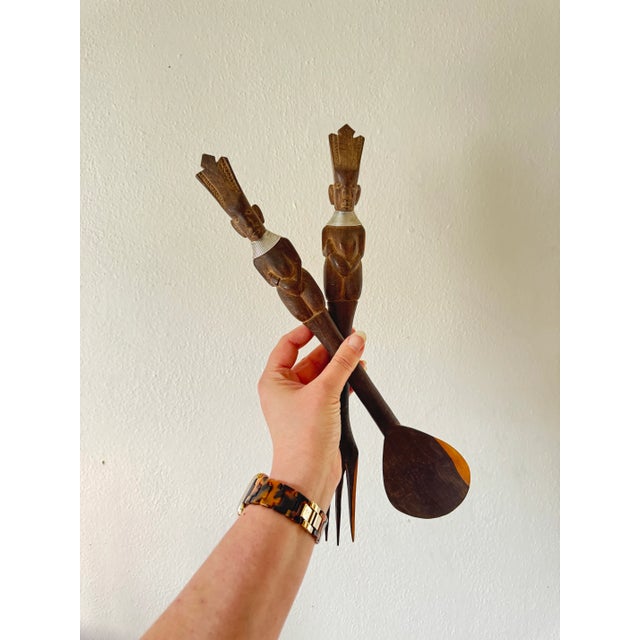 This lovely serving utensils feature figures wearing necklaces at the ends of each handle. They are made of carved wood...