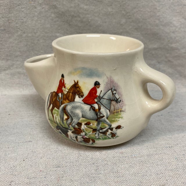 White ceramic mug depicting riders and hounds in a hunting scene. Designed to hold hot water in a lower chamber to keep...