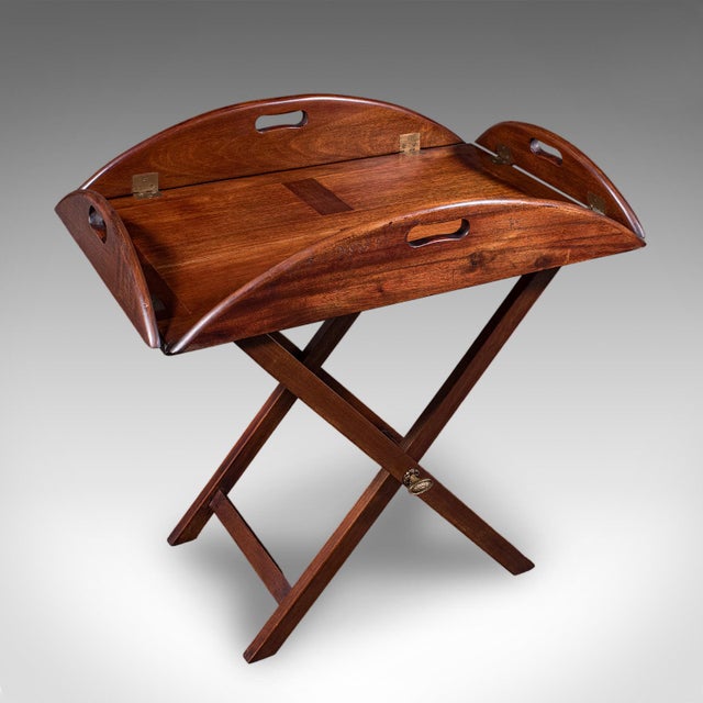 This is an antique butler's tray table. An English, mahogany and brass drop-flap serving stand, dating to the Edwardian...