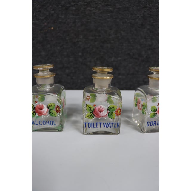 Four-piece Westmoreland glass vanity set featuring square clear glass bottles with hand-painted floral decoration in pink,...