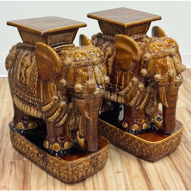 Vintage rich brown glazed elephant garden stools featuring decorative garb with tasseled headdress and saddle draping....