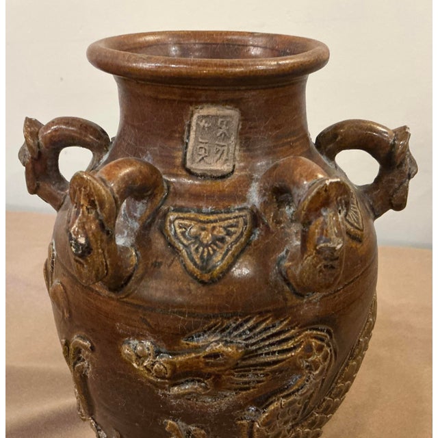 Features a high-fired stoneware body in dark brown and raised dragon motif. The lug handles at the top were used for...
