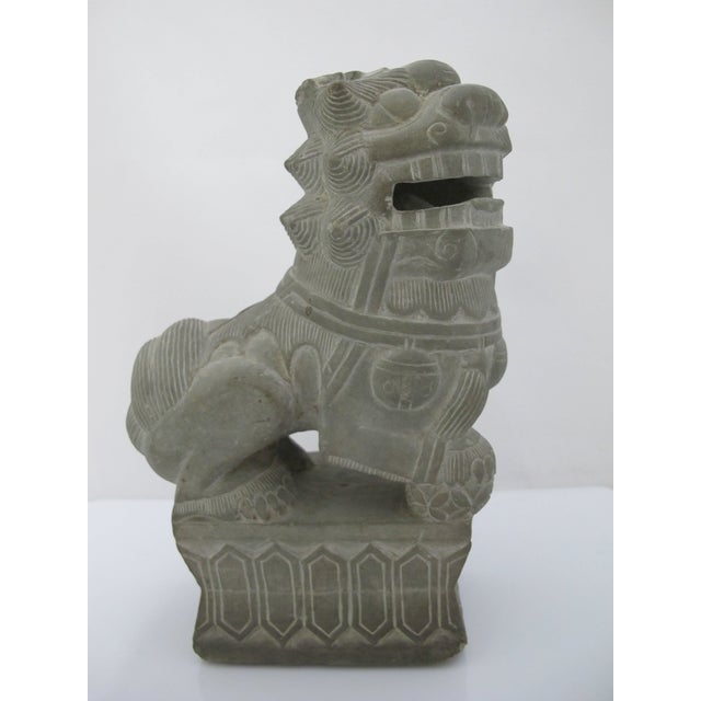 Carved stone Chinese guardian lion, or Foo Dog, featuring a stylized open mouth with ball inside and and ornate carved...