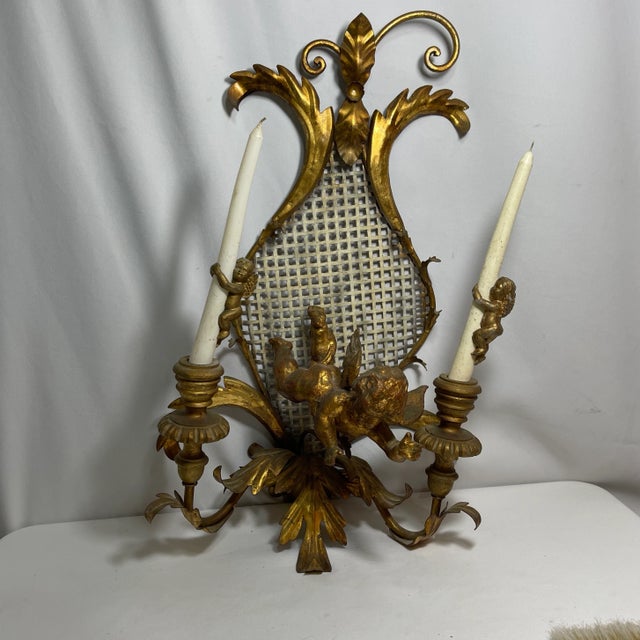 Gilded bronze sconces featuring a gliding cherub and floral designed frame. Two candleholders, as well as cherub candle...