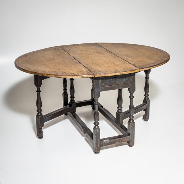 English drop-leaf table with an oval top and hinged leaves on both sides, supported by turned legs with stretchers. The...