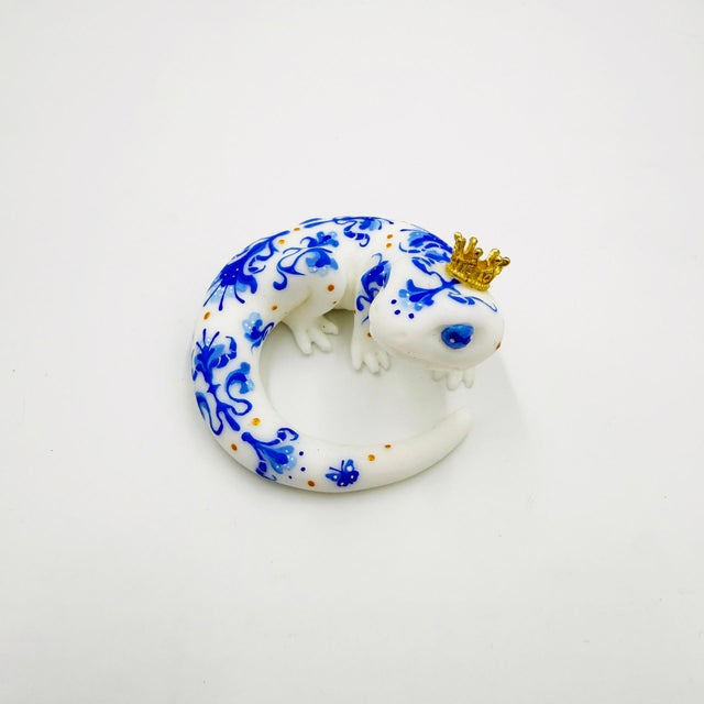 This resin cast artwork depicts a whimsical salamander adorned with intricate blue and white patterns reminiscent of...