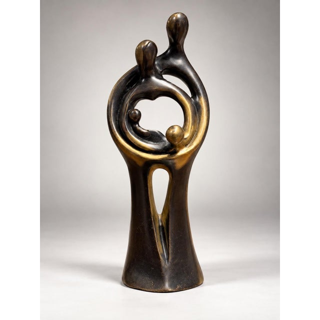 The object is an abstract bronze sculpture depicting an intertwined family group with polished high points and darker...