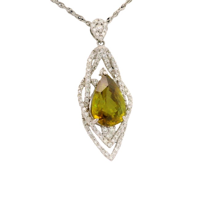 A captivating pendant showcasing a pear-cut green sphene, weighing 4.45 carats. The vibrant stone is encircled by 0.69...