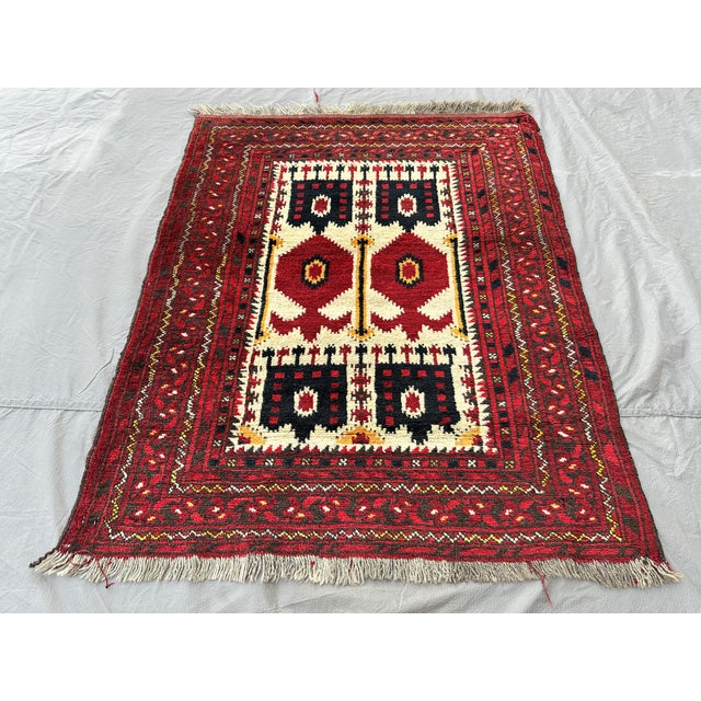 This small hand-knotted Baluch rug features two stacked rows of bold geometric medallions — checkerboard "flag" panels and...