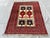 This small hand-knotted Baluch rug features two stacked rows of bold geometric medallions — checkerboard "flag" panels and...