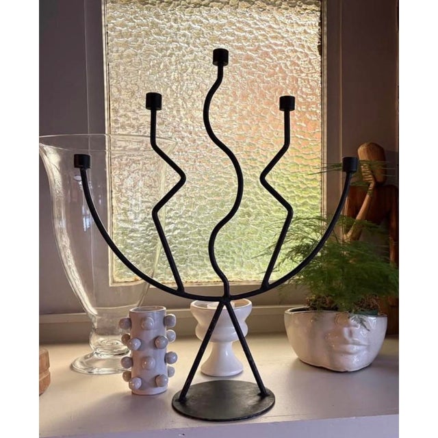 Striking sculptural candelabra crafted from blackened metal, featuring five gracefully curved arms with an organic, wave-...