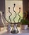 Striking sculptural candelabra crafted from blackened metal, featuring five gracefully curved arms with an organic, wave-...