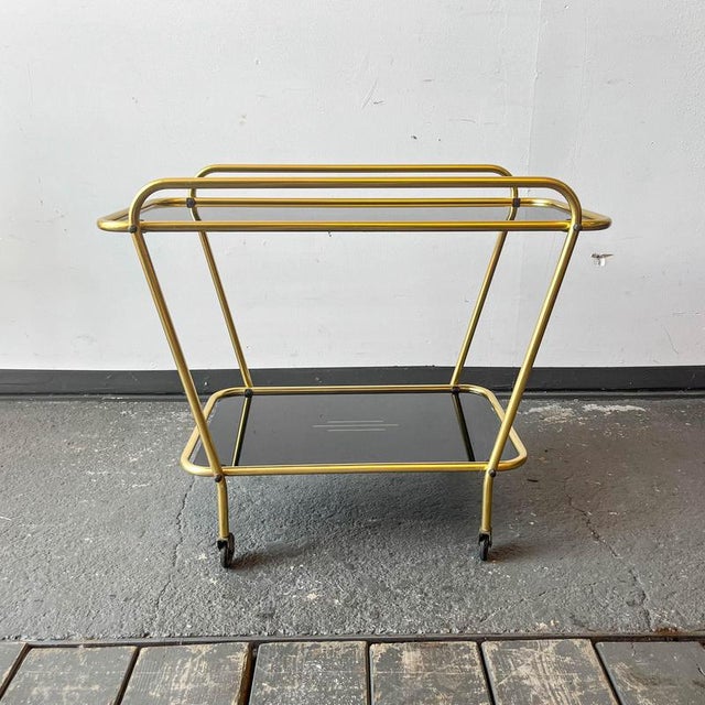 Product: serving trolley. Style: 1950s - 1970s. Material: brass frame, glass shelves, matte black. Features: two removable...