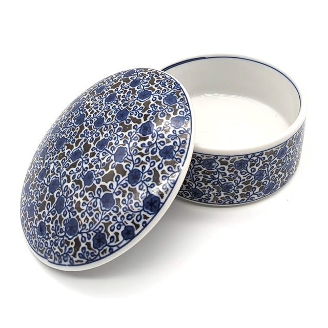 Offered is a round white porcelain trinket box embellished with a blue and brown floral pattern made in Japan in the late...