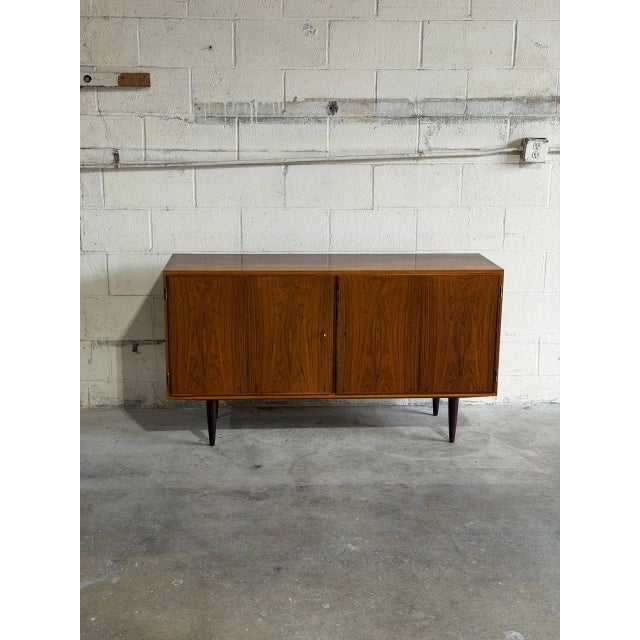 This minimalist low-profile credenza features a streamlined rectangular frame supported by dark tapered legs. The double...
