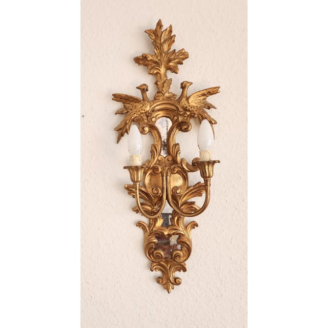 An exceptional pair of elegant antique rocaille wall lamps, crafted from gilded wood with original mirrored panels that...