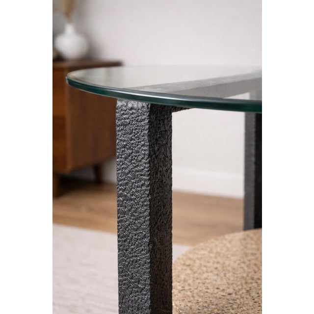 This sculptural vintage side table features a striking architectural form combining a thick round glass top, a textured...