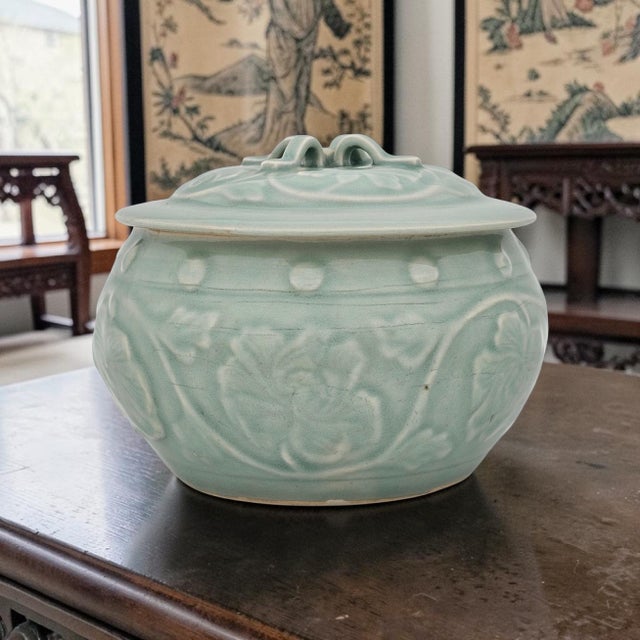 A Chinese Longquan-style celadon porcelain lidded jar featuring a rounded form with molded relief decoration of flowing...