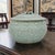 A Chinese Longquan-style celadon porcelain lidded jar featuring a rounded form with molded relief decoration of flowing...