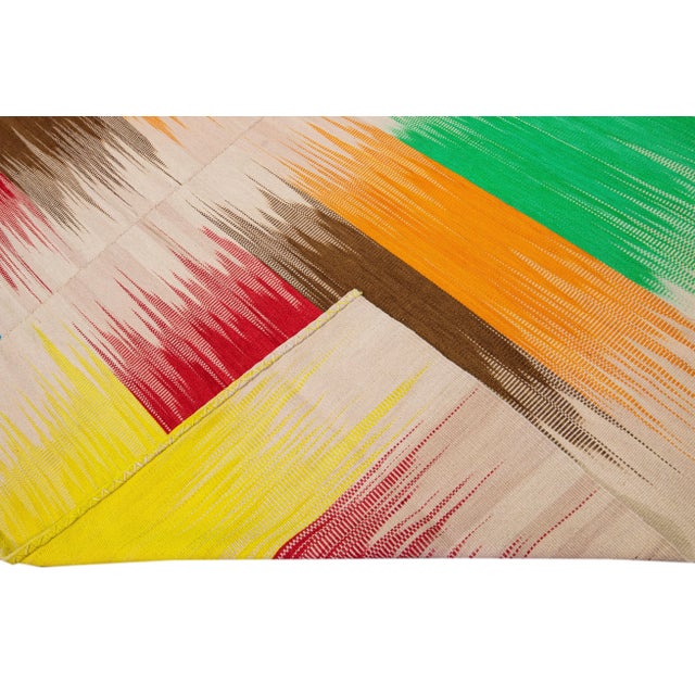 Beautiful modern Kilim flat-weave wool rug with a beige field. This piece of art has bright multicolor accents in a...