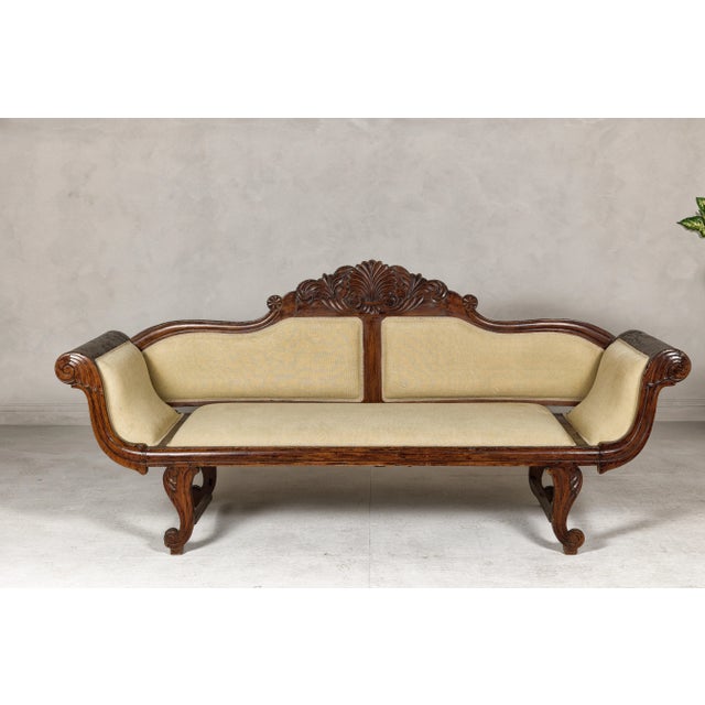 A Dutch Colonial period wooden settee from the early 20th century with carved crest, out-scrolling arms, cabriole legs and...