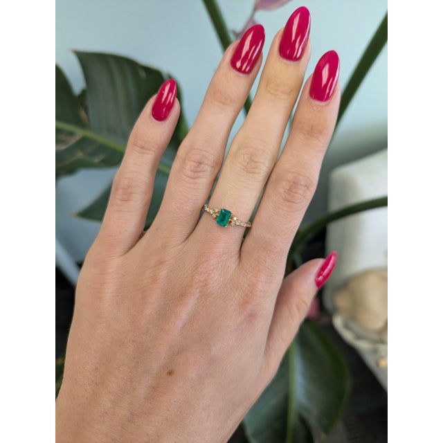 A Colombian emerald glows in vivid green at the centre of this solid 14K yellow gold ring, framed by ten earth-mined...