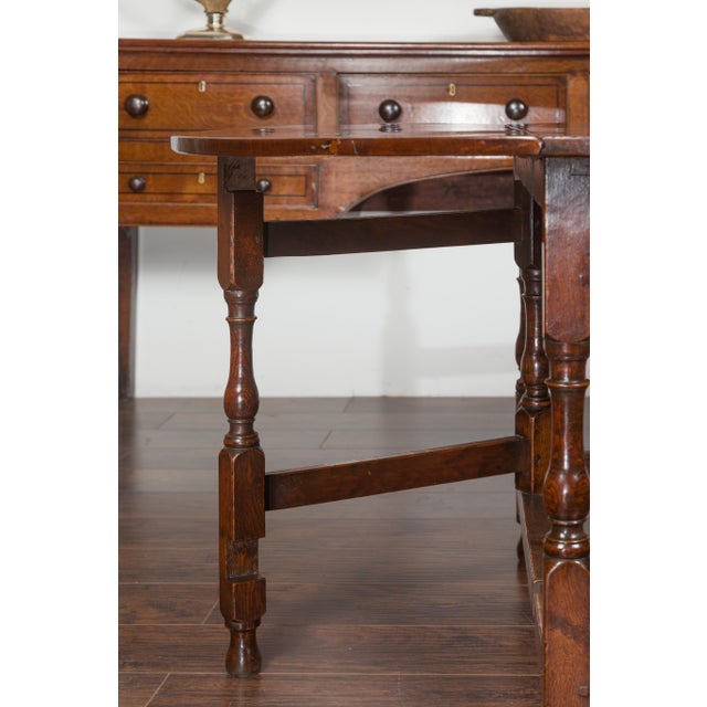 An English oak oval drop-leaf table from the late 19th century, with single drawer and baluster legs. Created in England...