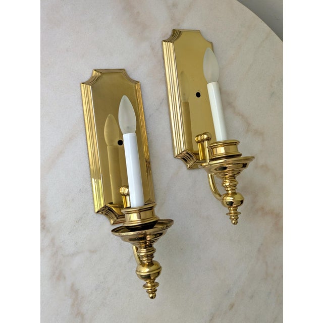 A pair of vintage French Provincial style electric wall sconces. The sconces feature a polished brass frame with a single...