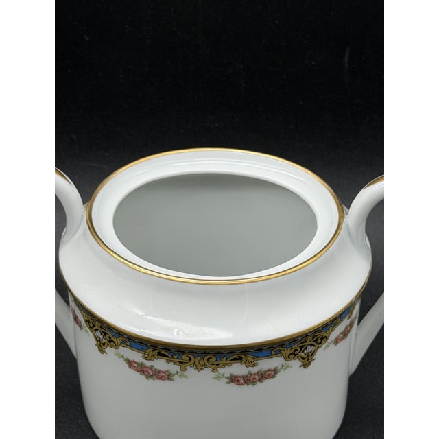 A 1950s Limoges tea set in white porcelain with a gold and blue decorative frieze featuring a pink floral motif. It...