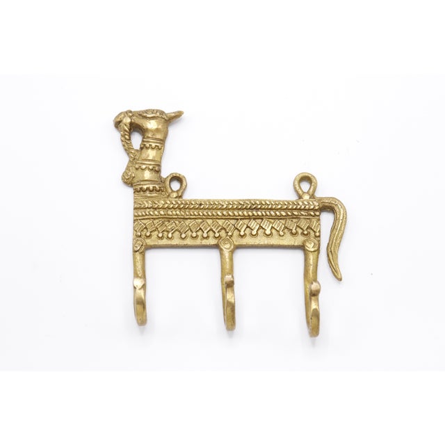 A bohemian brass wall fixture with three hooks. A central bar is cast with a camel head and tail and is decorated...