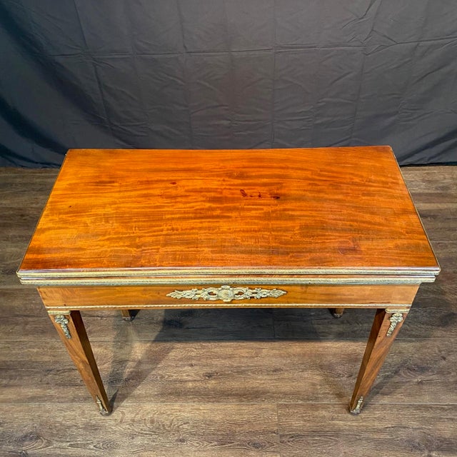 Elegant French Neoclassical game table crafted in richly figured wood with refined gilt-bronze mounts and slender tapered...