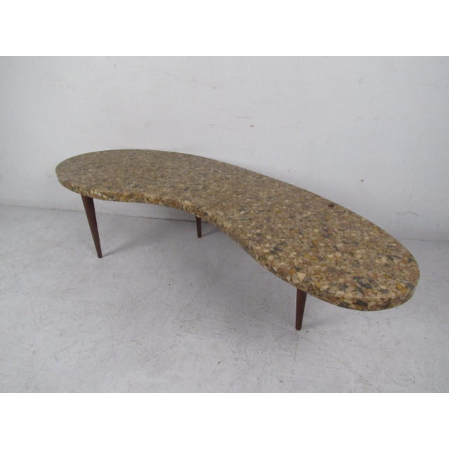 Vintage-modern kidney shaped coffee table featuring stone composite top and wooden base. Condition: age appropriate wear,...