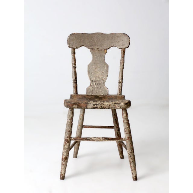 An antique primitive painted farmhouse chair featuring a shaped splat back, turned legs, and a beautifully aged painted...