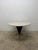 Arrowhead dining table with round natural 1.25” thick travertine top on a black lacquered steel and polished steel base by...