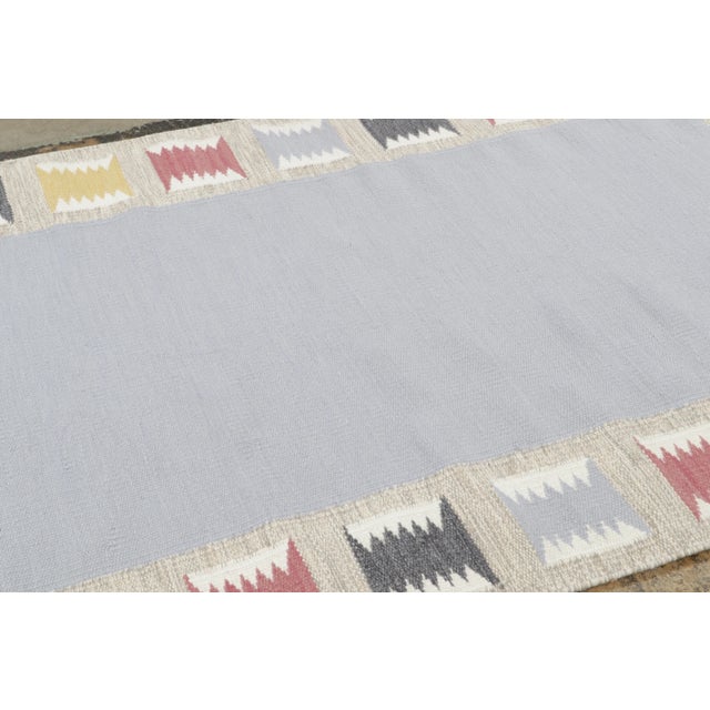 Handwoven in wool, this 5x8 Scandinavian rug showcases a minimalist field framed by rhythmic geometric motifs in sky blue,...