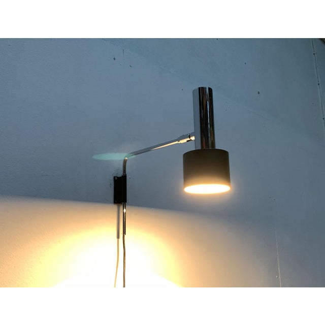 Mid Century wall lamp from Cosack in chrome and black. A minimalist design. The light head shows a simple radiant form...