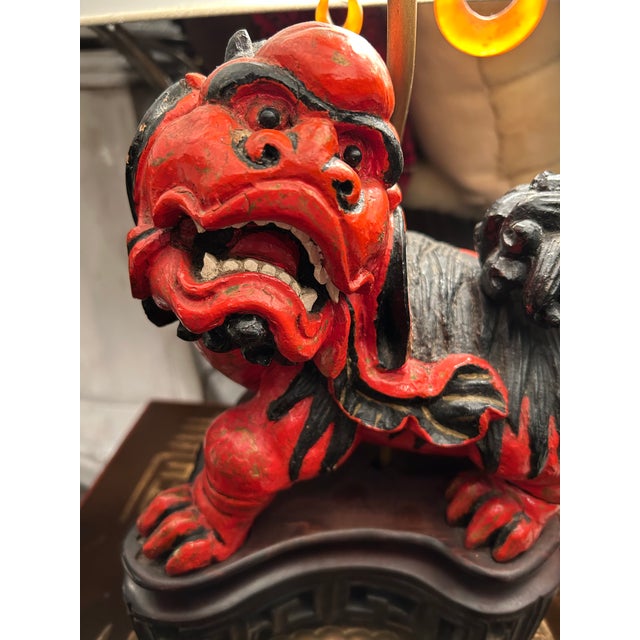 Dramatic pair of foo dog table lamps having red and black carved wood sculptures on cooper hand chased bases with figural...