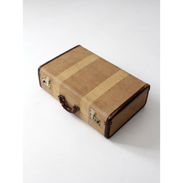 A 1930s vintage suitcase in woven canvas with soft striped banding and leather-trimmed edges. the compact form and warm,...