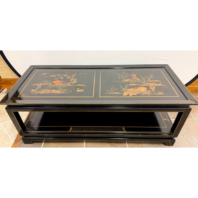 Chinoiserie black lacquered two tiered coffee table features hand-painted chinoiserie vignettes with figures, florals,...