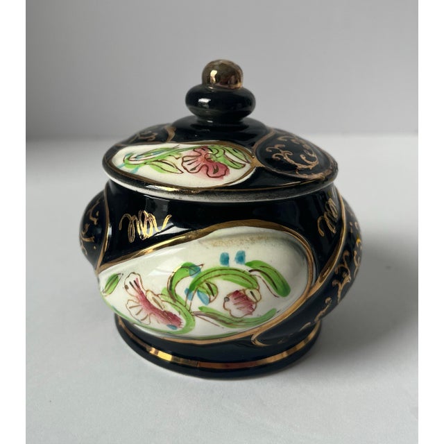 A vintage porcelain lidded sugar bowl by Norleans, made in Japan, featuring a dramatic black ground with hand-painted...
