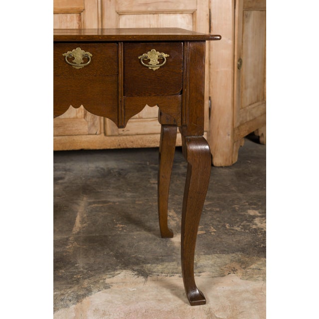 An English Georgian oak table from the 19th century with three drawers and cabriole legs. This English Georgian oak table...