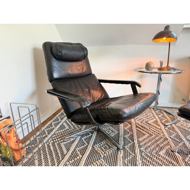 A generously sized mid-century lounge chair with matching ottoman, likely from the 1960s/1970s. It features black genuine...