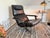 A generously sized mid-century lounge chair with matching ottoman, likely from the 1960s/1970s. It features black genuine...