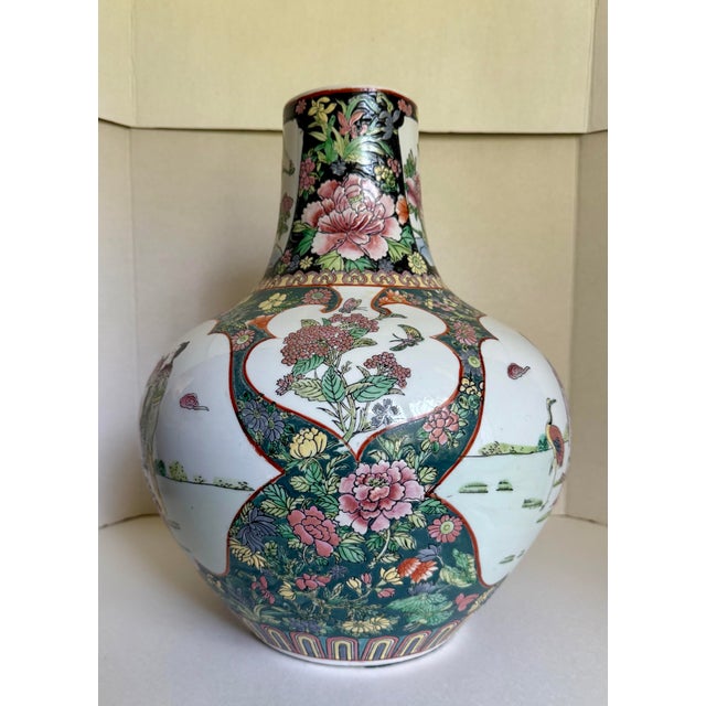 This statement Chinese porcelain vase features richly detailed scenes of court figures, cranes, peonies, birds, and other...