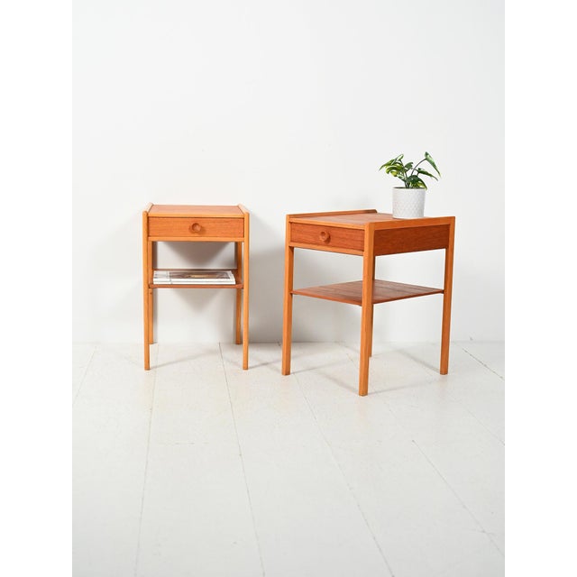 A pair of Scandinavian teak bedside tables, featuring a drawer and magazine shelf, elegant cantilevered profiles, and a...