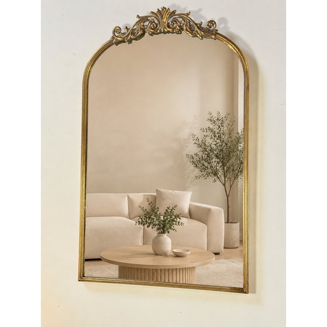 A gilt metal mirror from the 2000s. Its arched shape is topped by a tall pediment decorated with scrolls and floral...